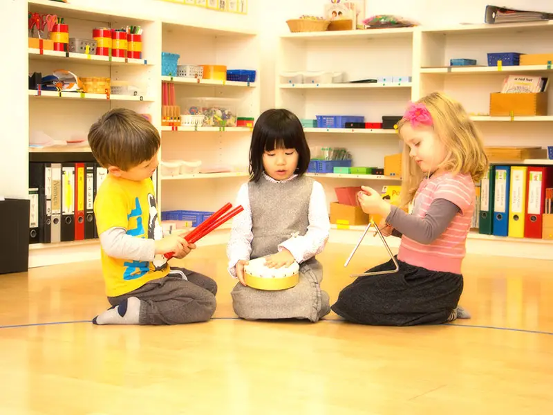Drei Kinder musizieren gemeinsam mit Tamburin, Klanghölzern und Triangel