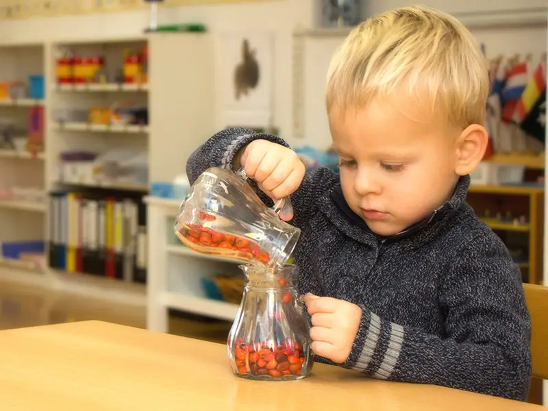 Kind gießt konzentriert Perlen um und arbeitet selbstständig mit Montessori-Material