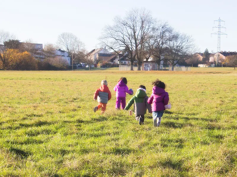 Kinder laufen gemeinsam über eine Wiese in der Umgebung des Kindergartens